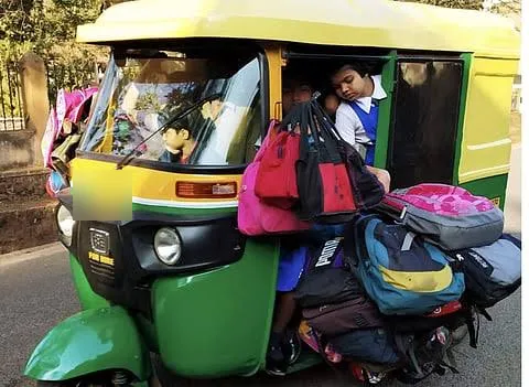 School auto-rickshaw with schoolbags hanging off the sides and a child squeezed against the open doorway