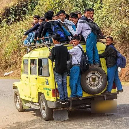 More than a dozen students riding on the roof and hanging off the back of a yellow school jeep